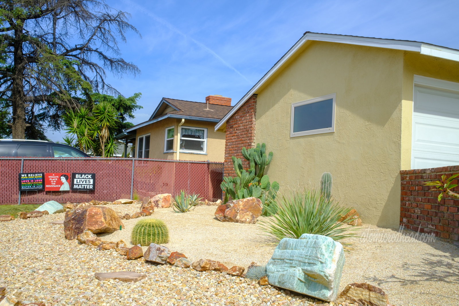 A rock pathway weaves toward the house, edged with large rocks. Cacti sit between the path and the house.