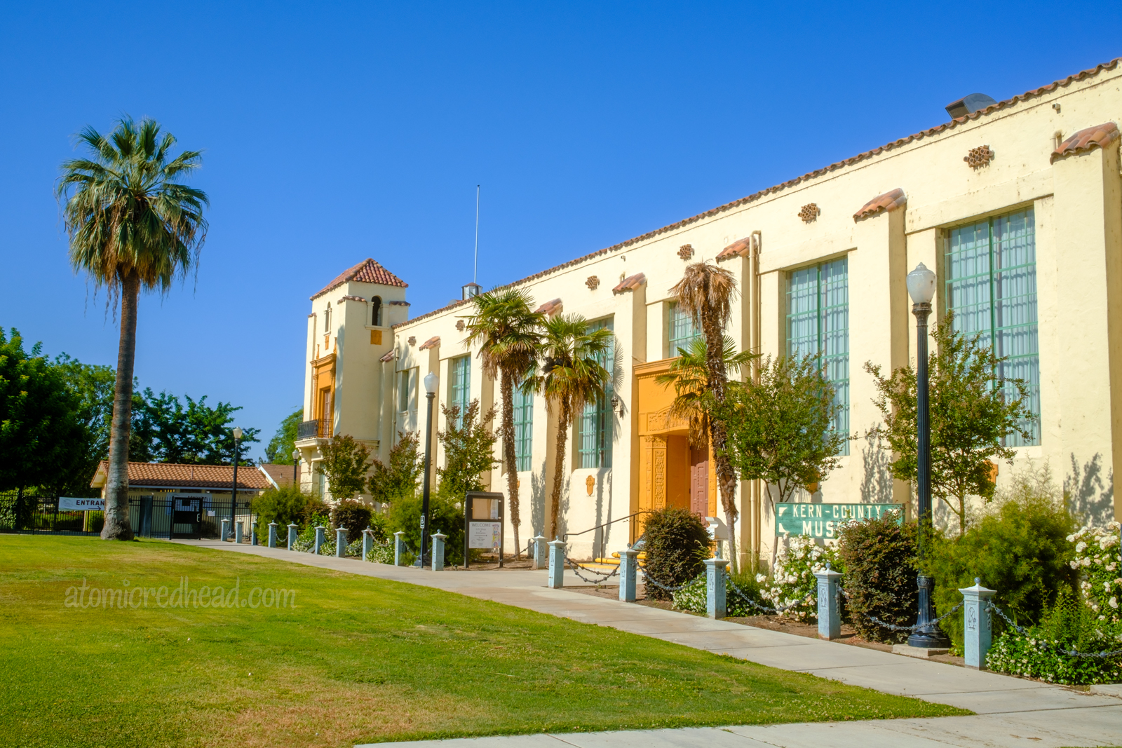 Exterior of the Kern County Museum, a long Spanish Colonial revival style building with red tile roof, and palm trees out front.
