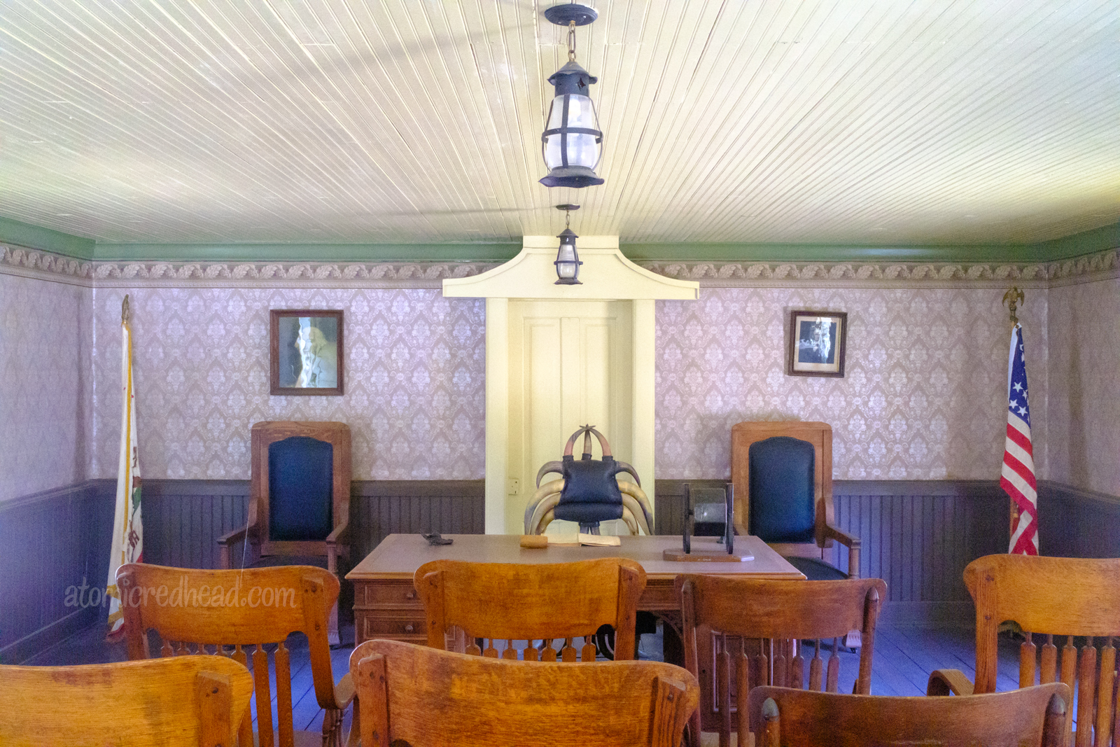 Interior of the old Kern County Court House. Purple wallpaper surrounds a chair made of cattle horns, that is behind a desk. Dark wood chairs reside in front.