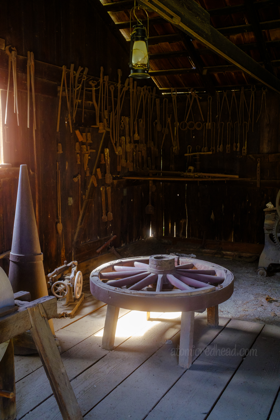 Inside of the blacksmith shop. A variety of tools line the walls, a wagon wheel sits awaiting repair.