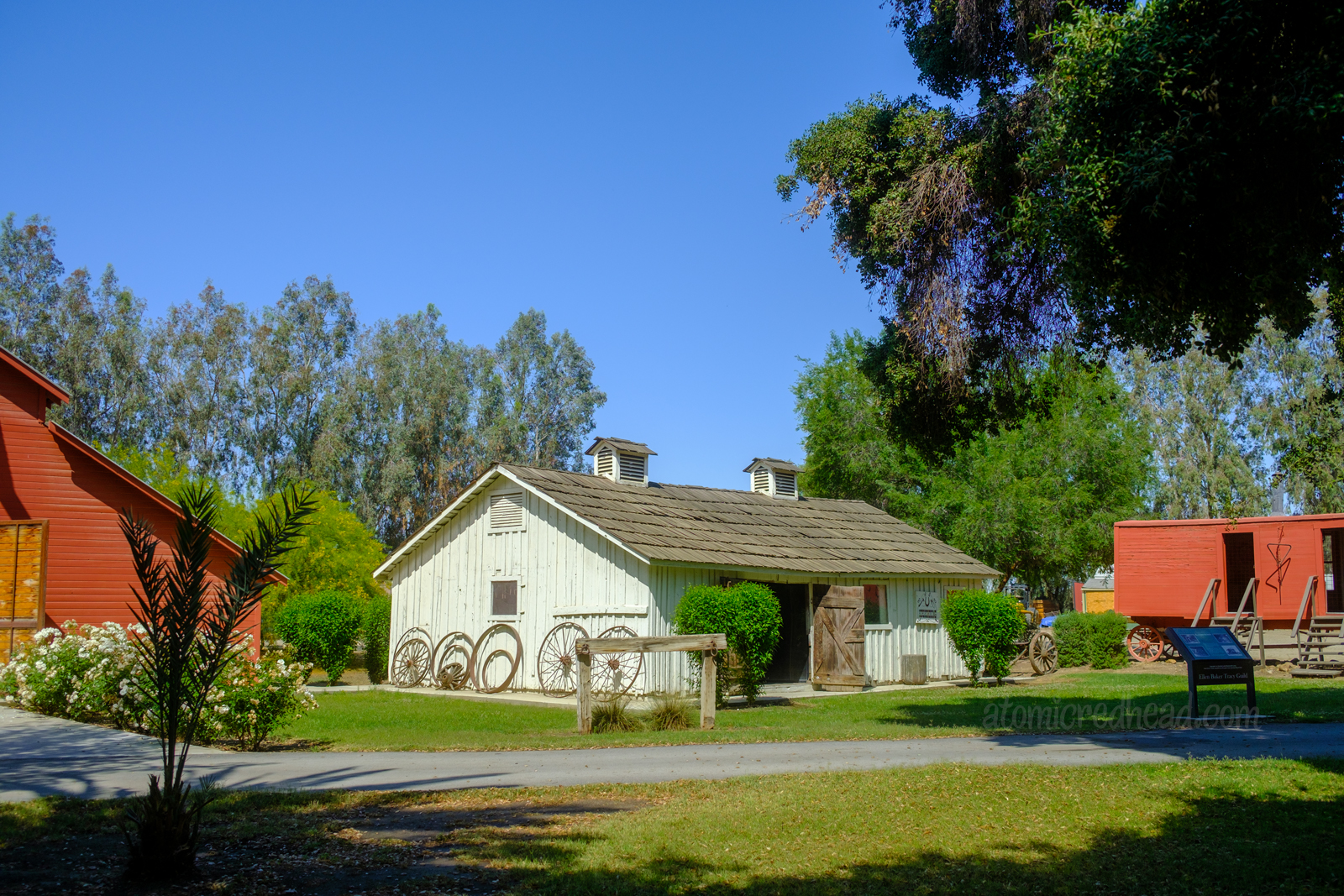 Exterior of the blacksmiths shop, a long white building. An array of wagon wheels sit along the side.