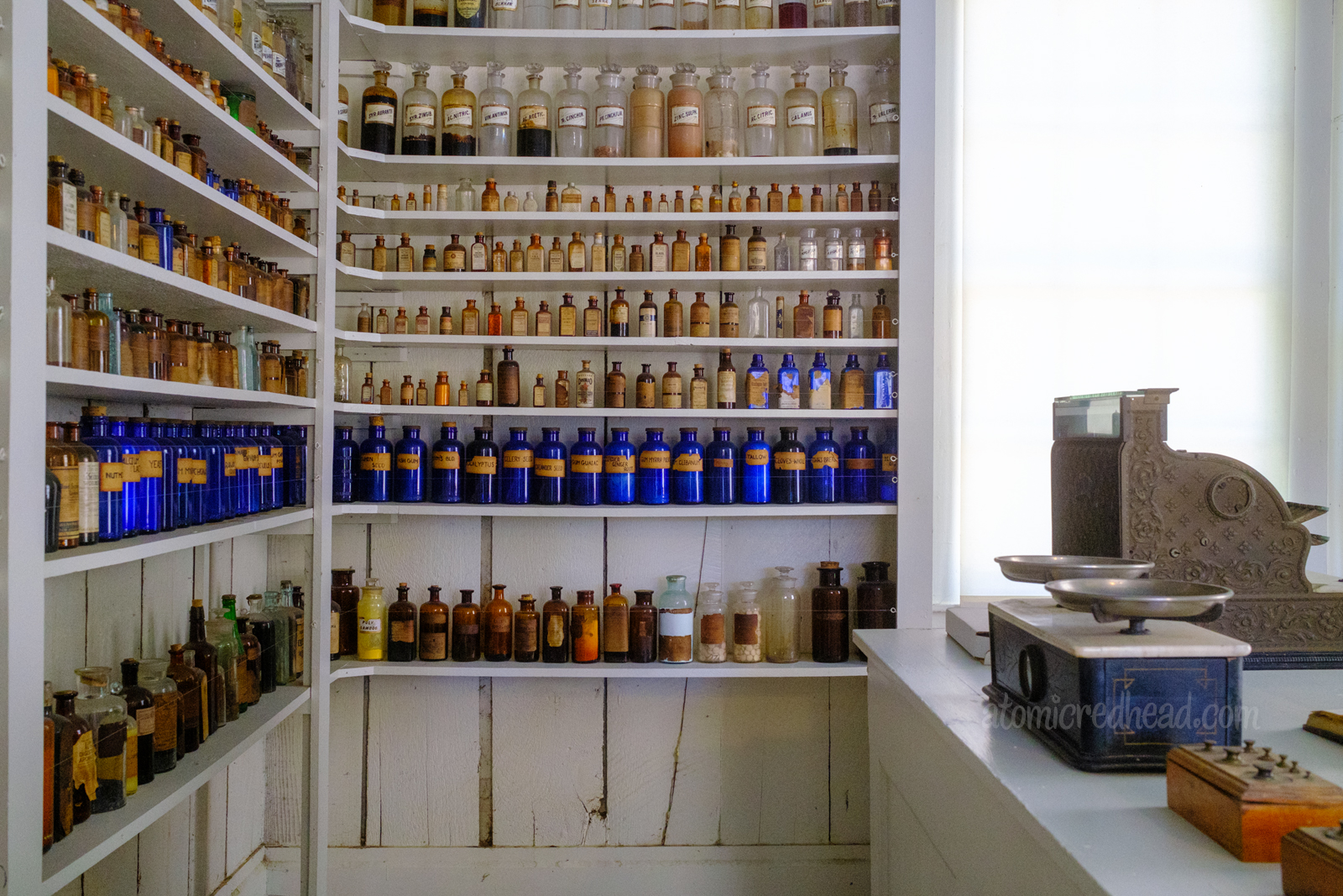 Inside the drug store, where a wide selection of glass bottles sit on shelves. Some are clear, others blue, and some brown.