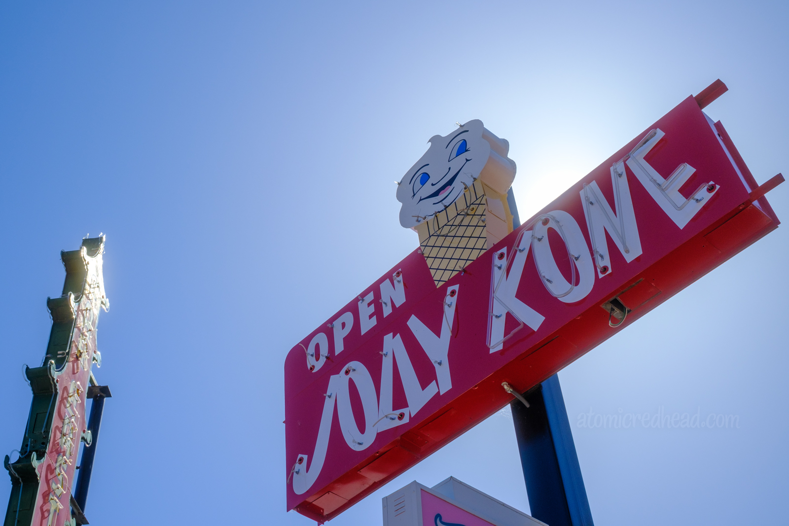 A red neon sign with white letters reading "Open Jolly Kone" and a small ice cream cone on top, with a face on the ice cream.