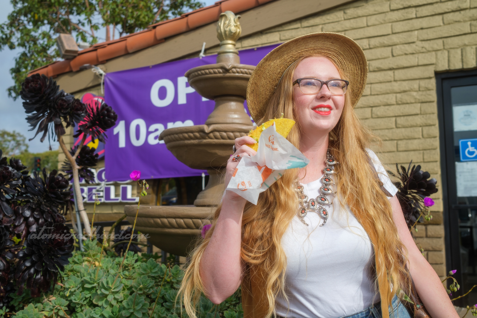 Myself outside of the Taco Bell, holding a crunchy taco, with a fountain in the background