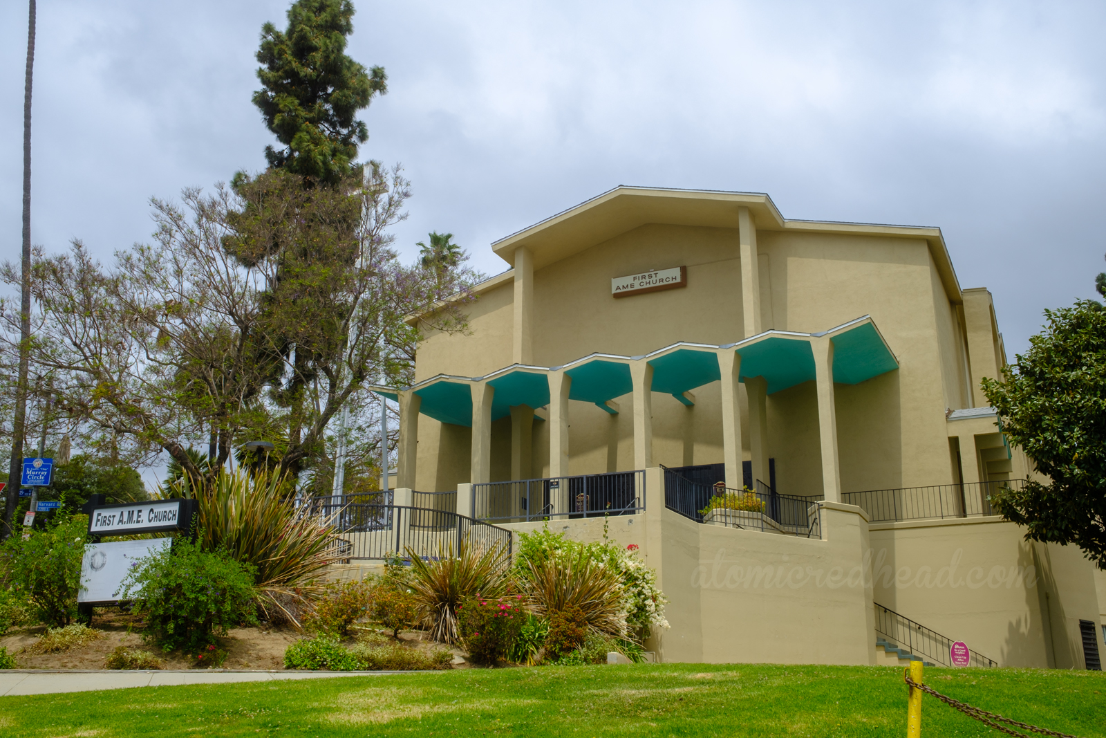 A pale yellow church with zig-zag roof that juts out over the doors, the underside painted turquoise. The sign reads "First AME Church"