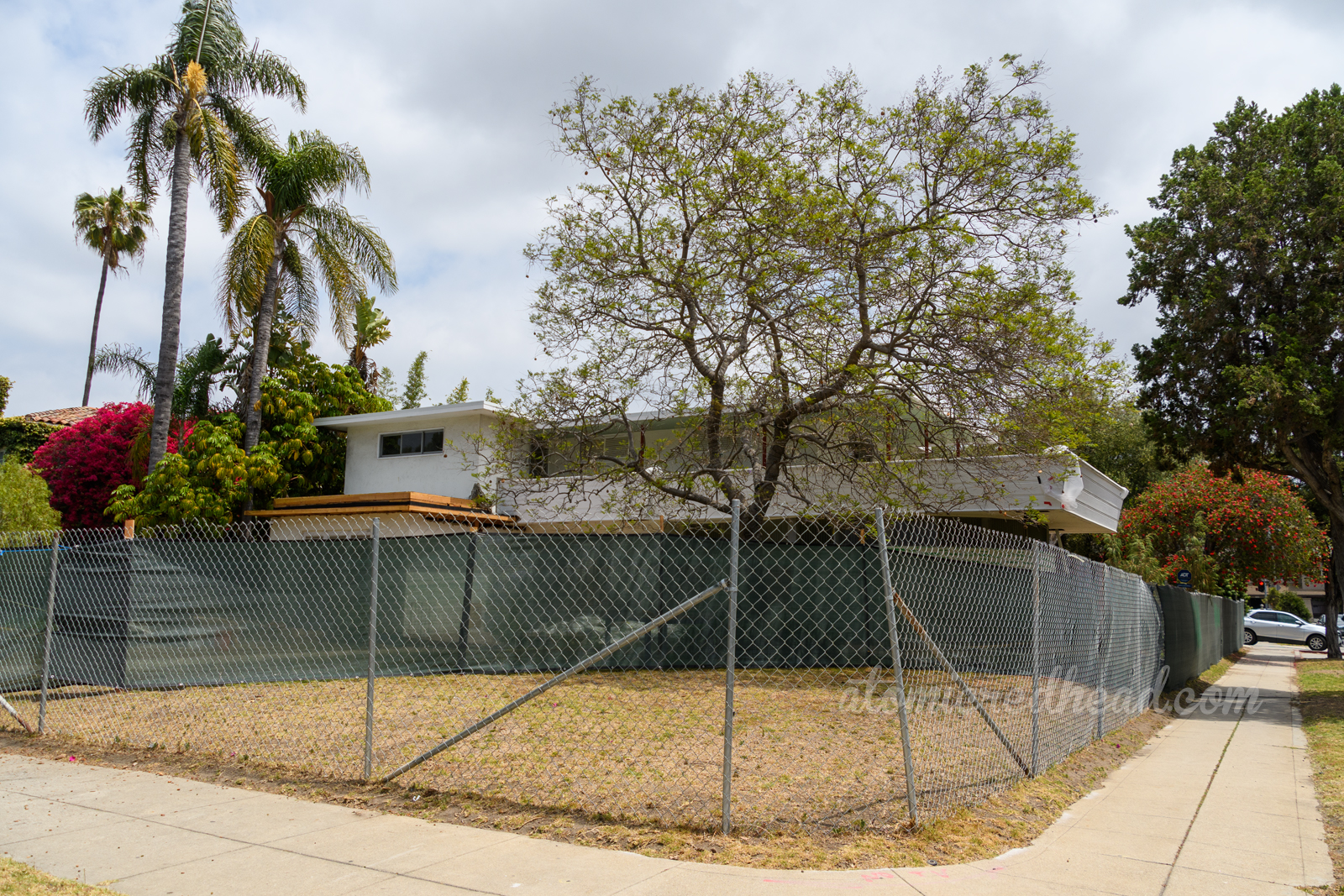 A mid-century modern home peeks out over a covered chain link fence.