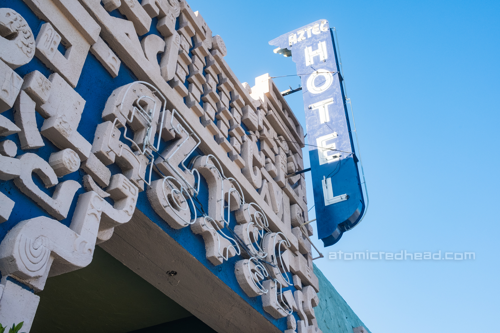 Entrance to the Aztec, which reads "Aztec Hotel" above the doorway and on a blade style neon sign painted blue and white.
