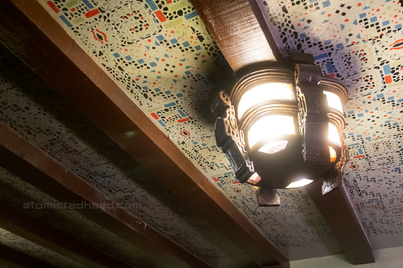 A carved wooden light fixture hangs from a heavily pattern ceiling.