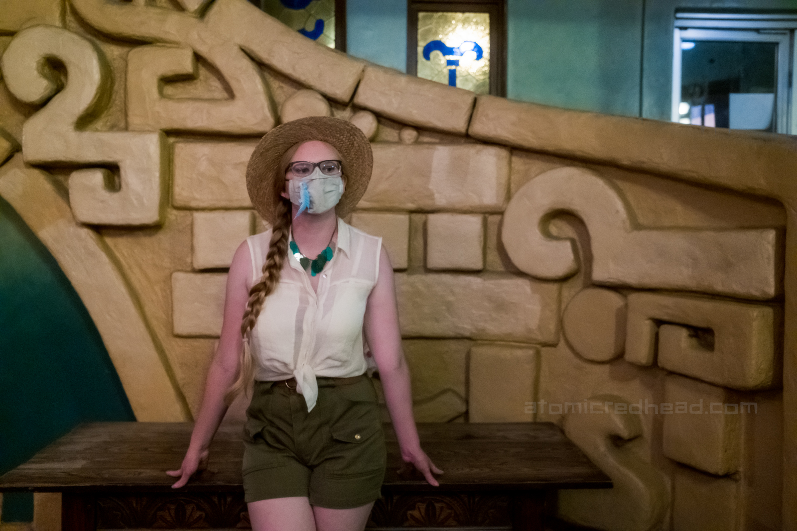 Myself, wearing a straw hat, white sleeveless blouse and green shorts, standing in front of the staircase.