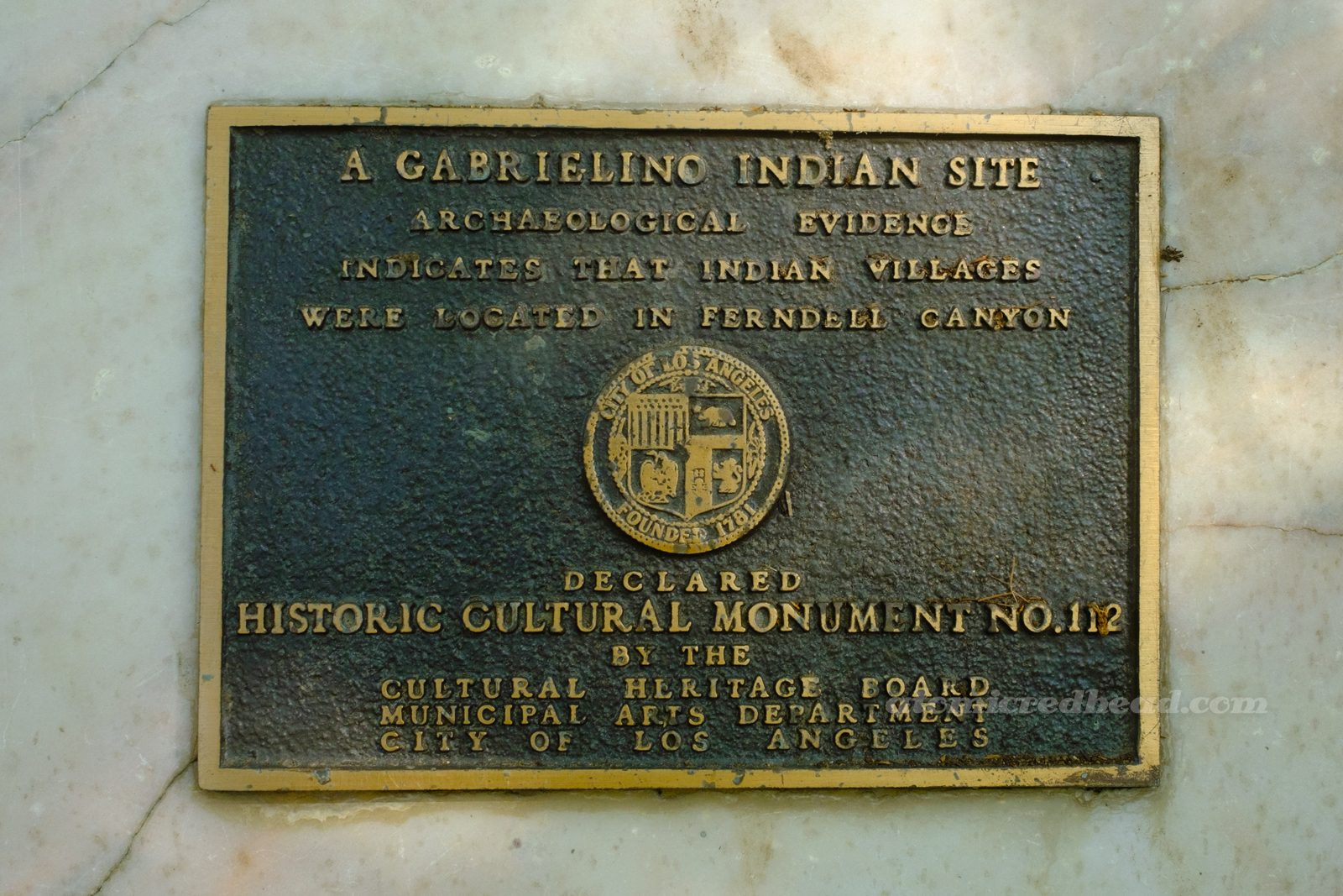 A bronze plaque reading "A Gabrielino Indian Site. Archaeological Evidence indicates that Indian Vilages were located in Ferndell Canyon. Declared Historic-Cultural Monument No. 112 by the Cultural Heritage Board Municipal Arts Department City of Los Angeles."