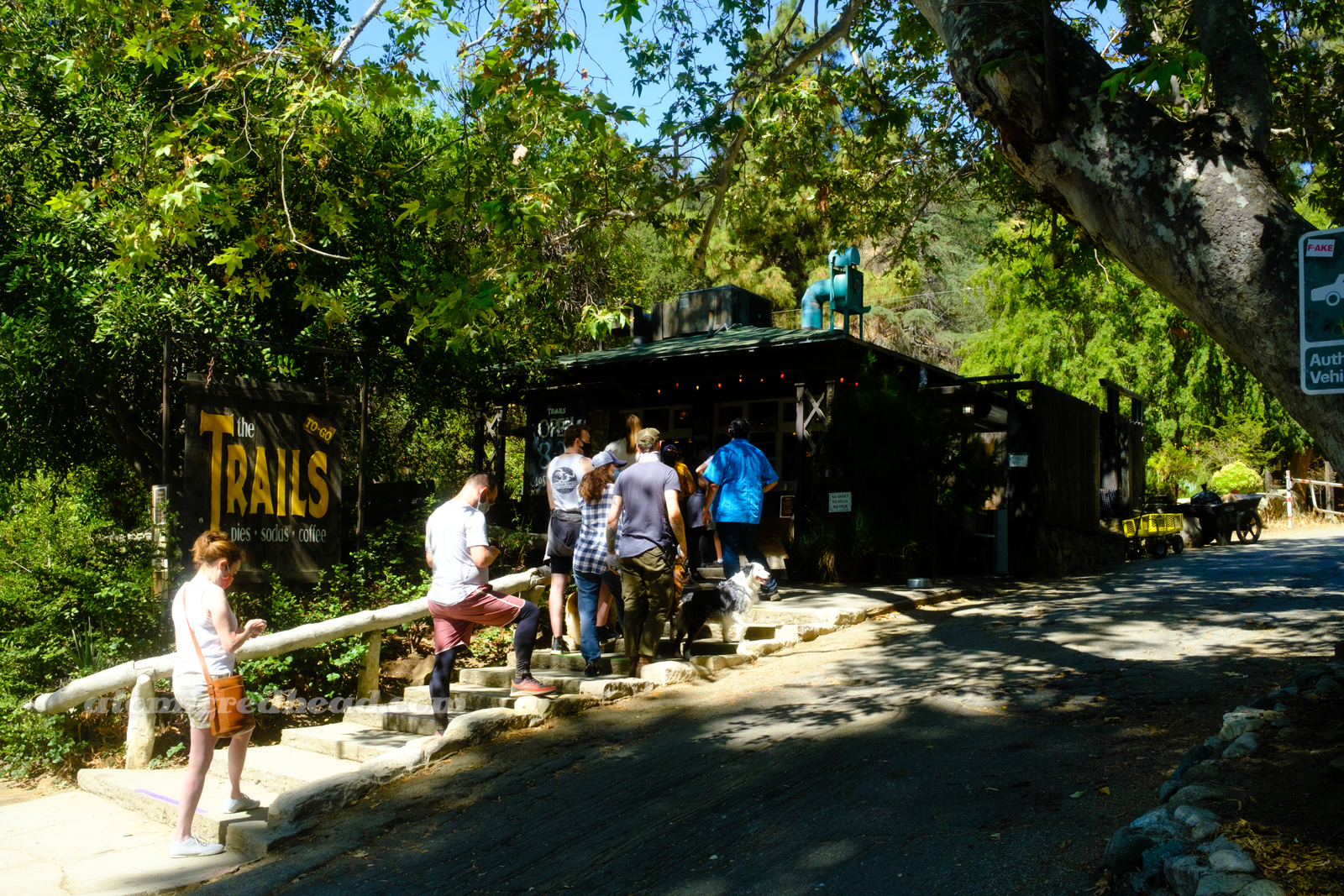 Exterior of The Trails, a small wooden building with a line of people waiting to order.
