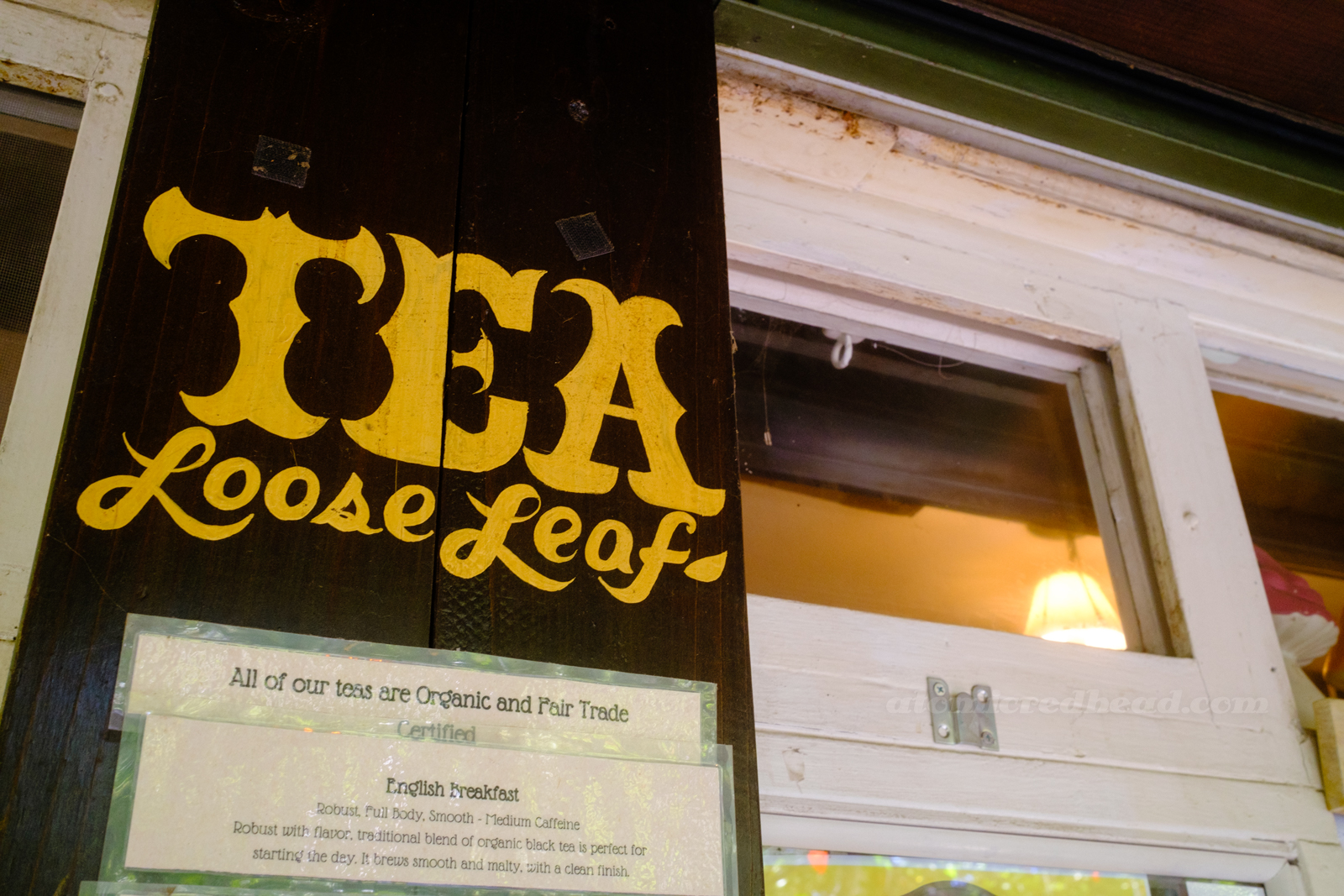 Yellow script hand-painted on wood reads "Tea Loos Leaf" in yellow letters.