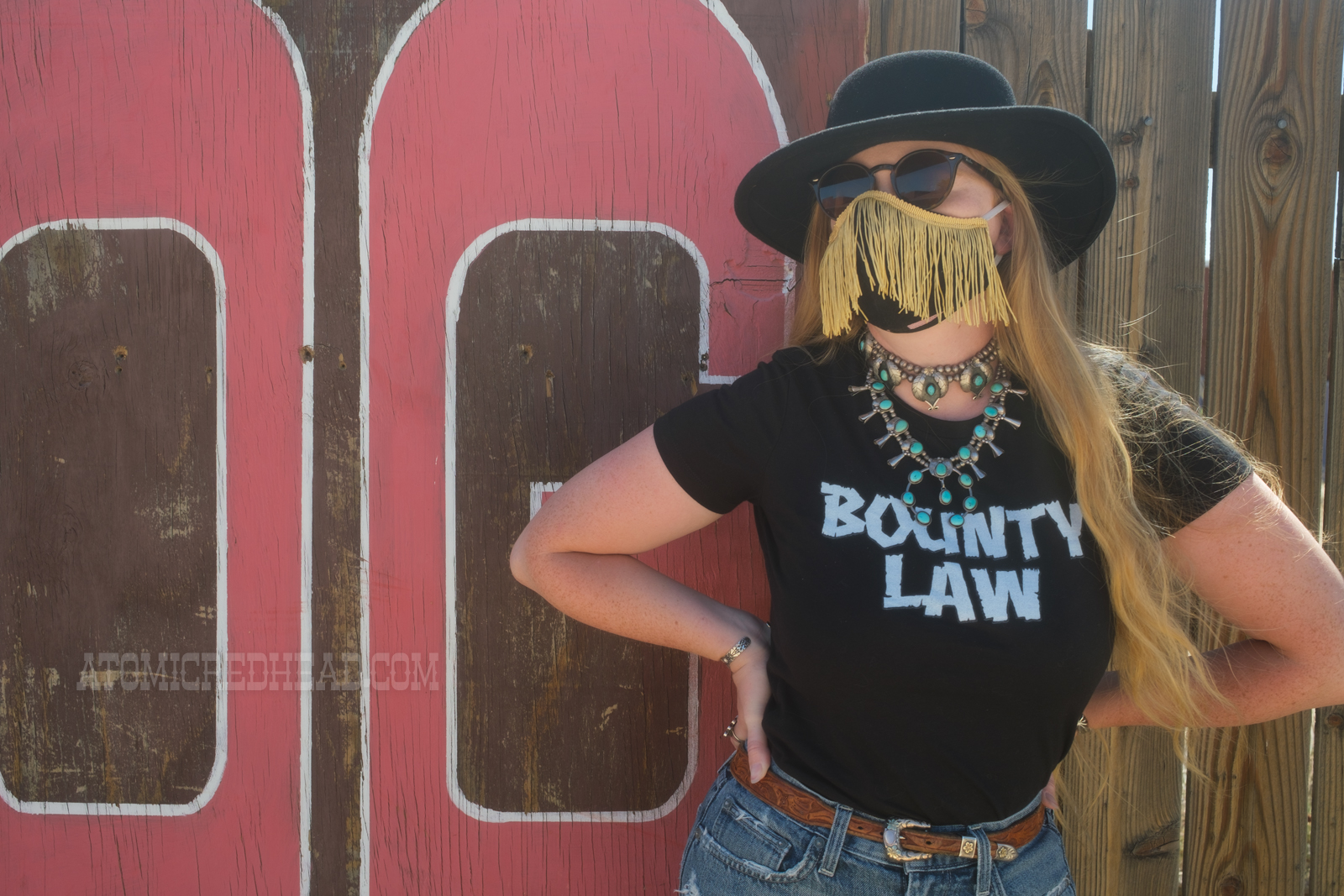 Myself, wearing a black cowboy hat, black tee reading "Bounty Law" and jean shorts, leaning against a large sign reading "The Red Dog" in large red letters.