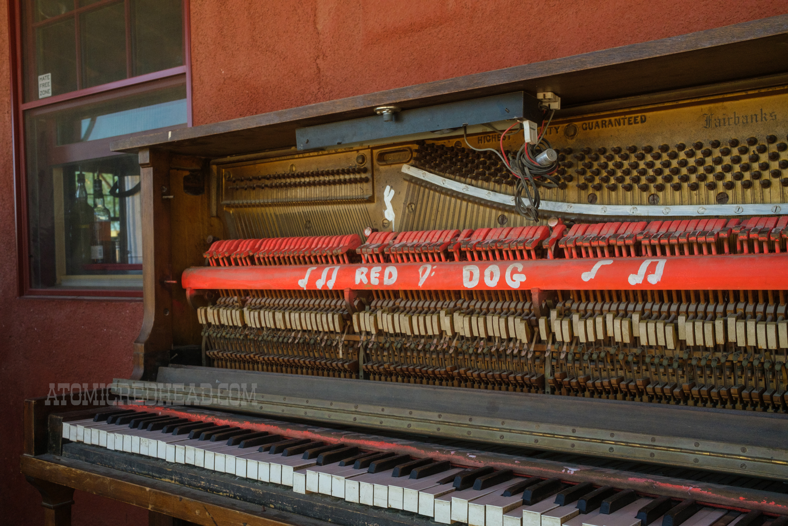 An old piano sits on the porch, painted on it reads "Red Dog"