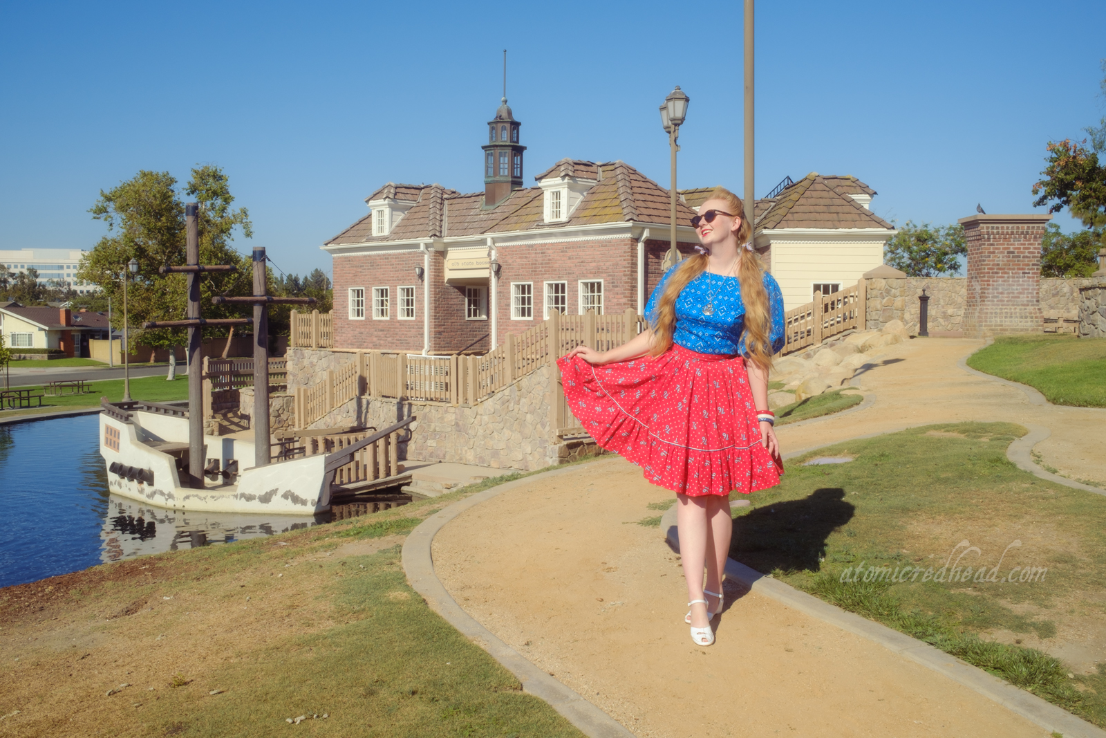 Myself, wearing a blue peasant top with a bandana print on it, a red skirt with "76" in white scattered throughout, and white shoes, standing in front of an old New England style building.