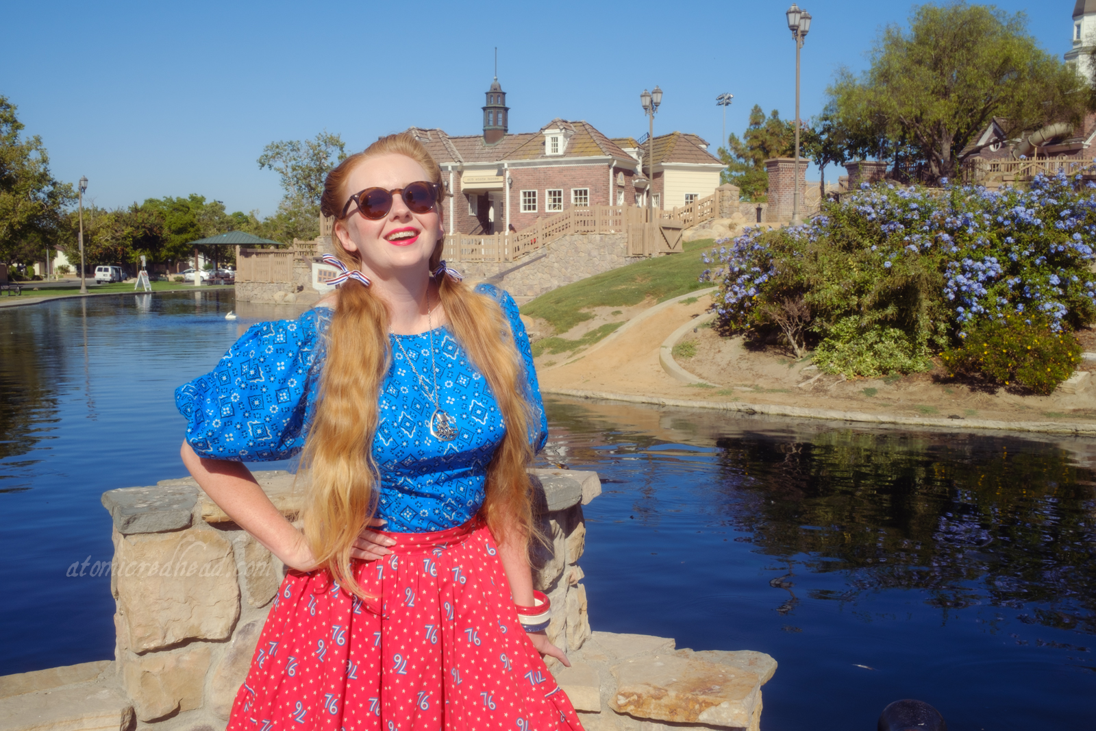 Myself, wearing a blue peasant top with a bandana print on it, a red skirt with "76" in white scattered throughout, and white shoes, standing in front of an old New England style building.