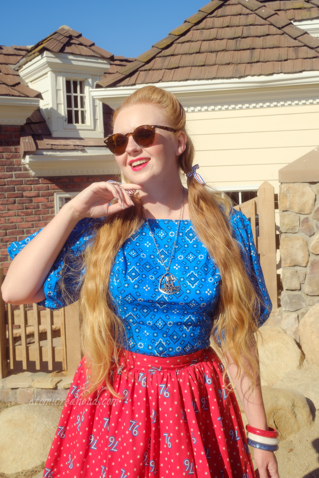 Myself, wearing a blue peasant top with a bandana print on it, a red skirt with "76" in white scattered throughout, and white shoes, standing in front of an old New England style building.
