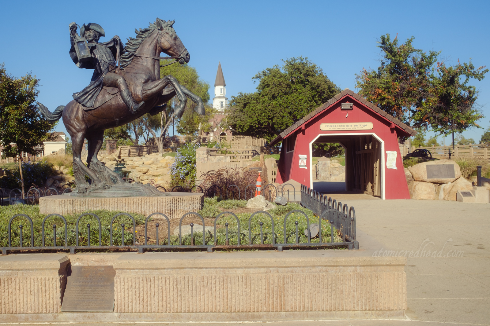 A statue of Paul Revere atop a rearing horse stands in front of a small covered bridge which gives way to the small New England themed island.