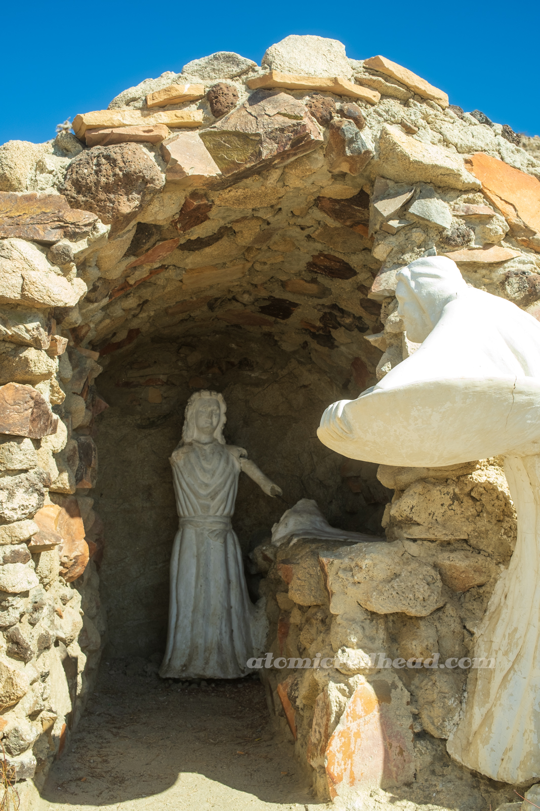 A small statue, that has broken parts of its arm over the years, sits within a small cave.