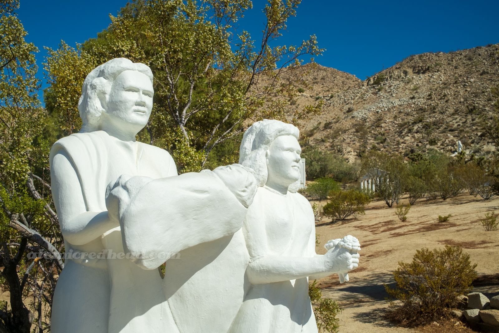 Close-up of two statues, one carries a baby, another carries a small bouquet of flowers.