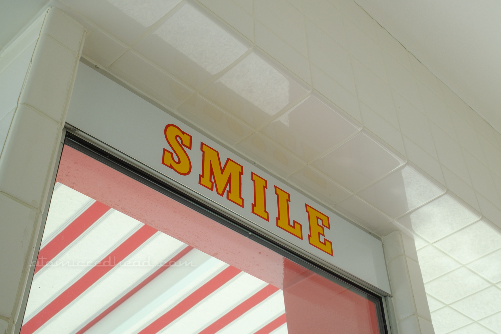 Close-up of yellow letters edged in red reading "Smile" located above the service window.
