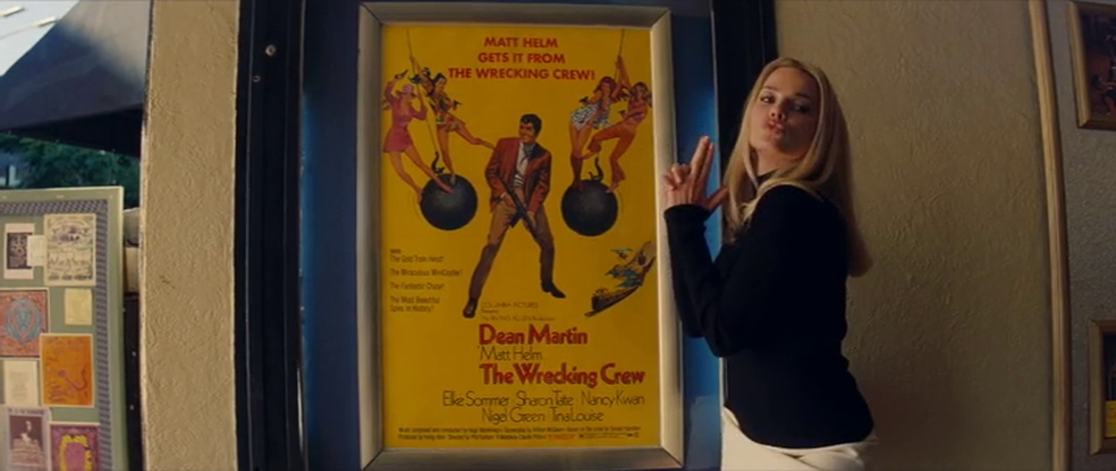 Robbie as Tate poses next to the poster for The Wrecking Crew.
