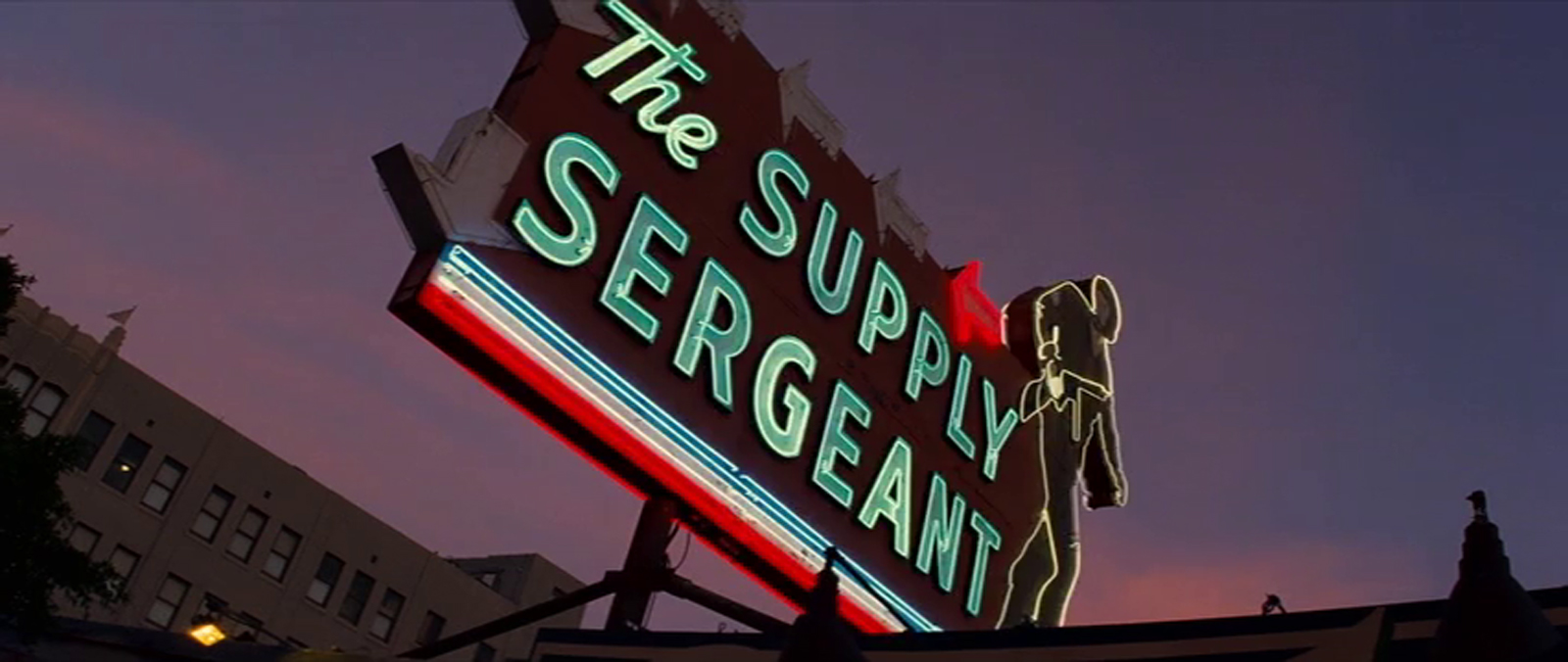 The Supply Sergeant as it appears in Once Upon a Time...In Hollywood, lit up at night, with a neon soldier, red neon arrows, and blue neon reading "The Supply Sergeant"