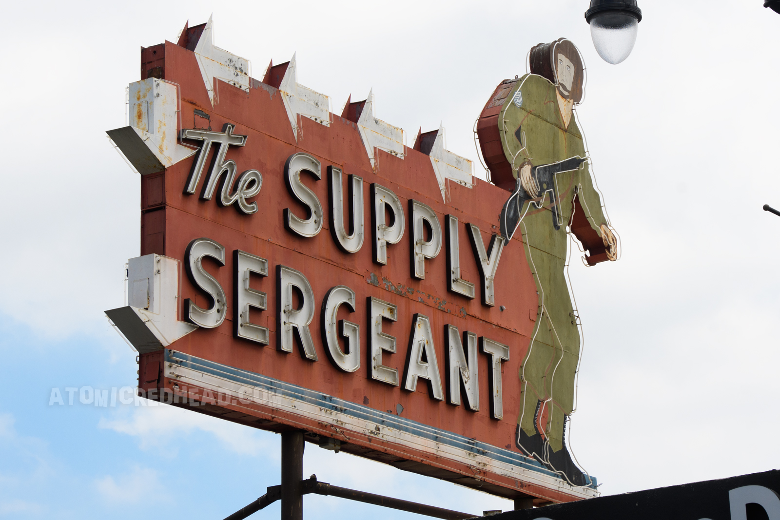 The Supply Sergeant as it appears today, during the daytime, with a massive told neon soldier on the right, and text reading "The Supply Sergeant" in white letters.