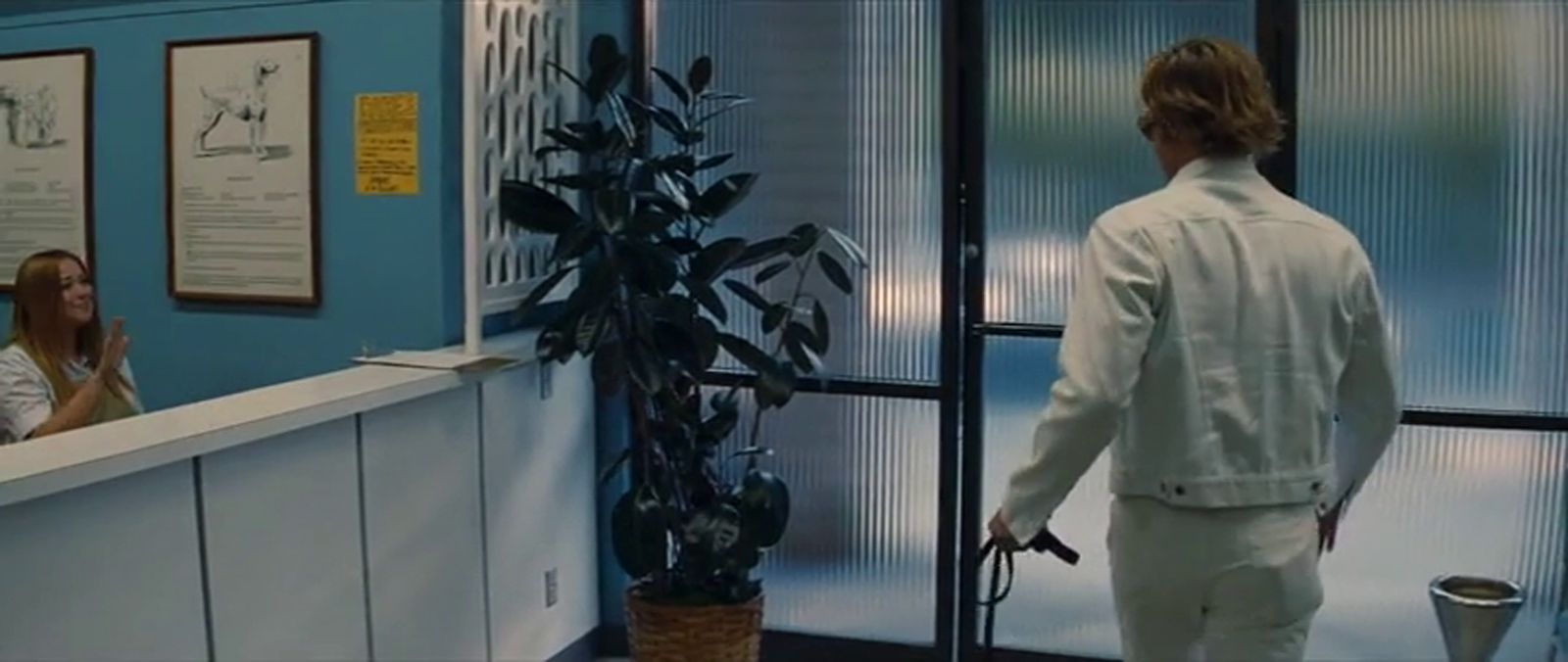 Cliff, dressed in a white jean jacket and white jeans, has his dog, Brandy, by the leash. The check in counter of the vet sits on the left, with blue painted walls. Wall to wall, floor to ceiling frosted glass makes up the front portion of the lobby.