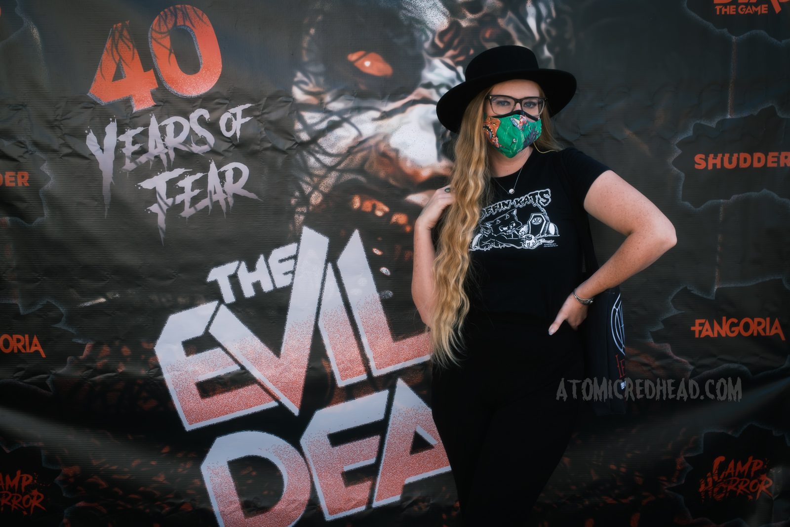 Myself, wearing a black cowboy hat, a Koffin Kats tee, and black pants, standing in front of a large banner reading "40 Years of Fear The Evil Dead" featuring the Deadite version of Cheryl.