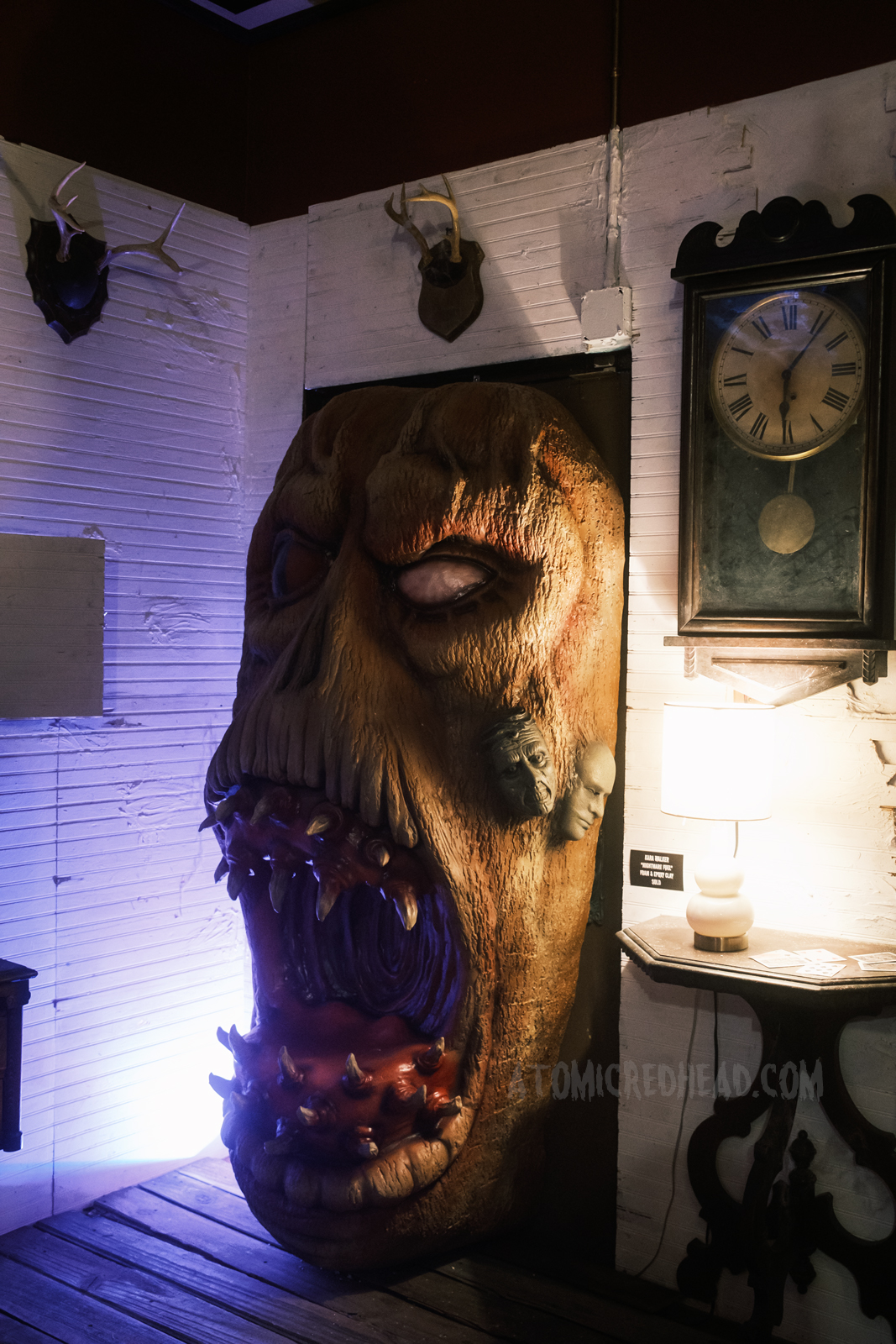 A massive Deadite face pushes its way through a doorway, an antique clock hangs on the wall to the right.