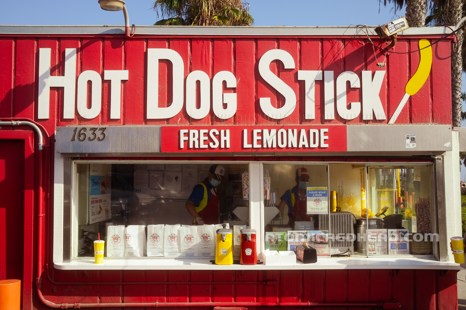 The side of the location, a red building with a long window in the middle. White text along the top reads "Hot Dog Stick Fresh Lemonade" with a small image of a corndog on the right.