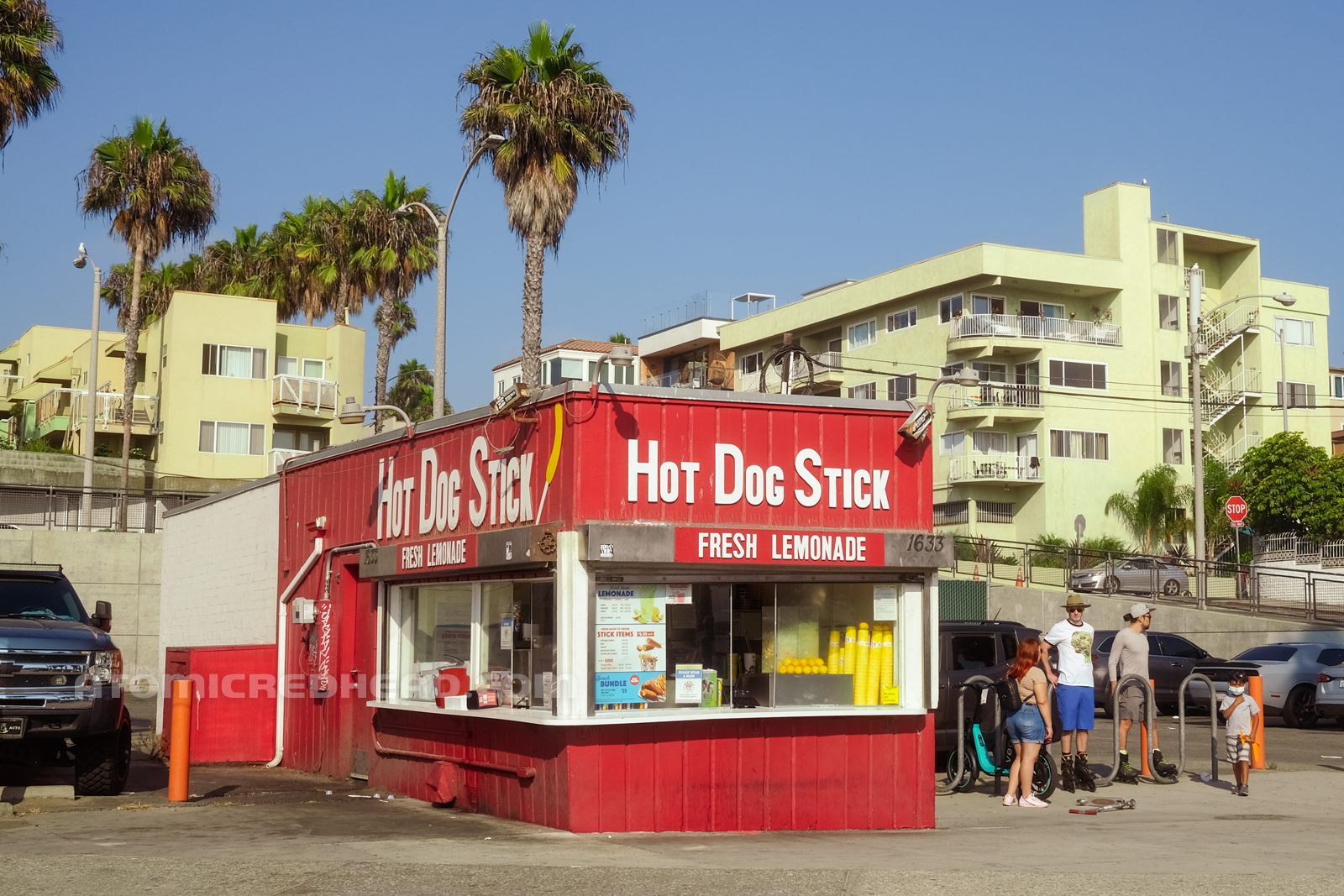 Three-Quarter view of the stand, painted red with its name in white letters. Stacked yellow cups sit int he window with lemons next to them.