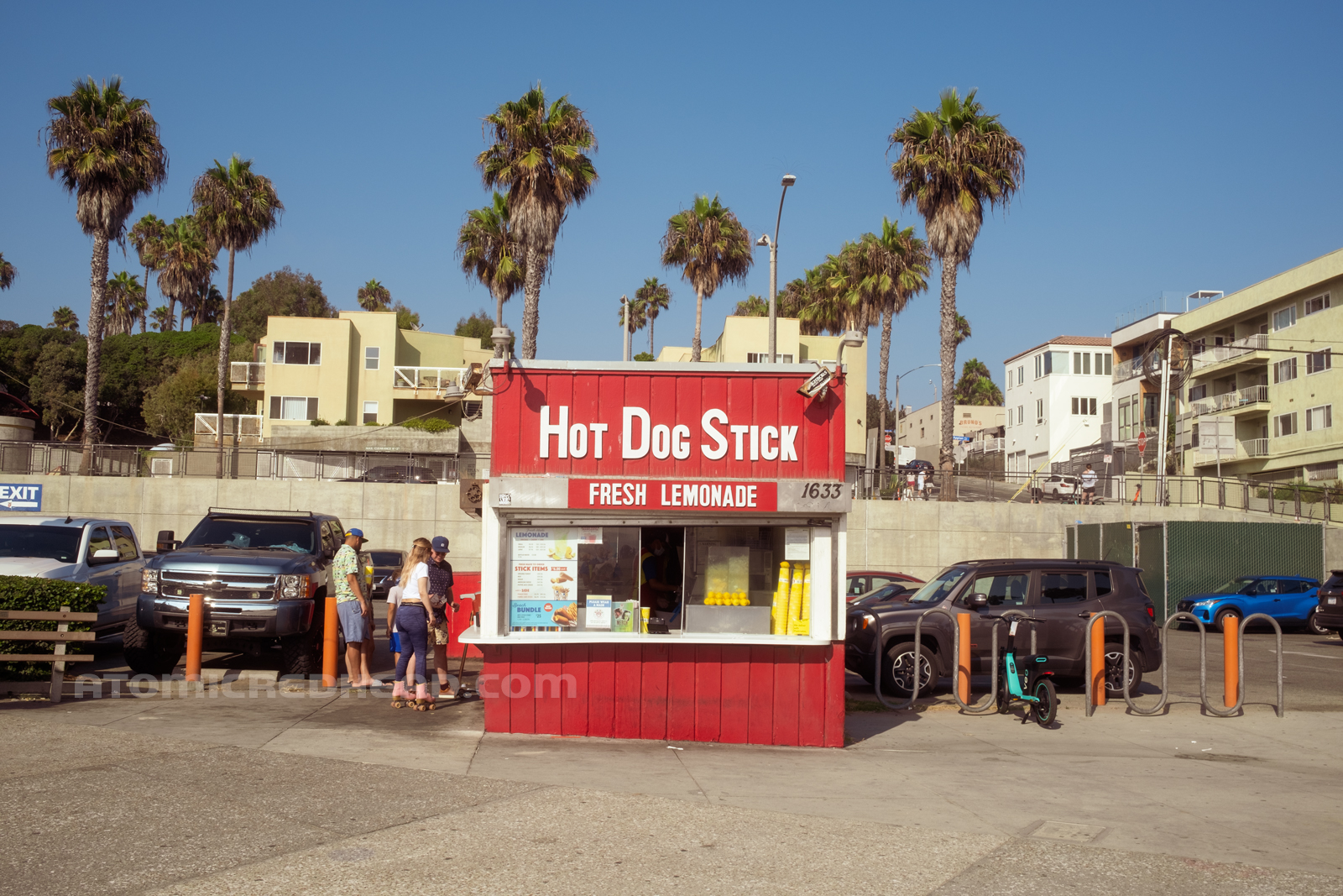 Front of the building, mainly painted red, with a white service window, and white letters reading "Hot Dog Stick Fresh Lemonade."