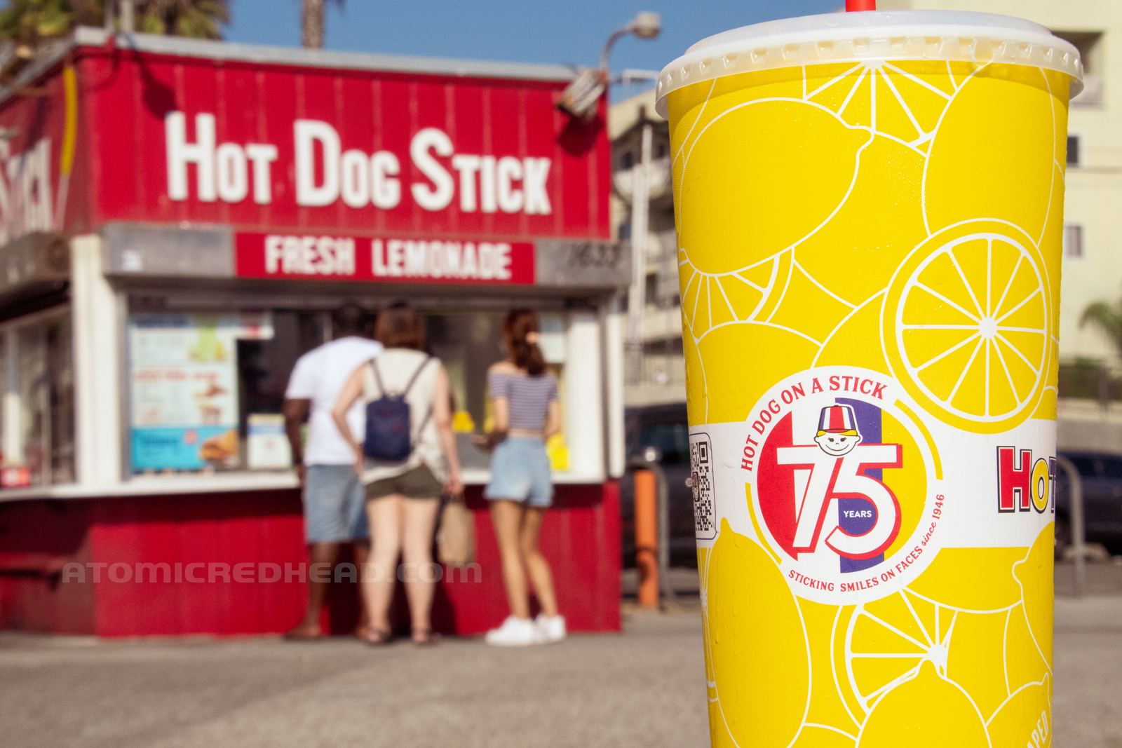 In the foreground, a yellow cup features the 75th anniversary logo, and text reading "Sticking Smiles on Faces since 1946." the building in the background.