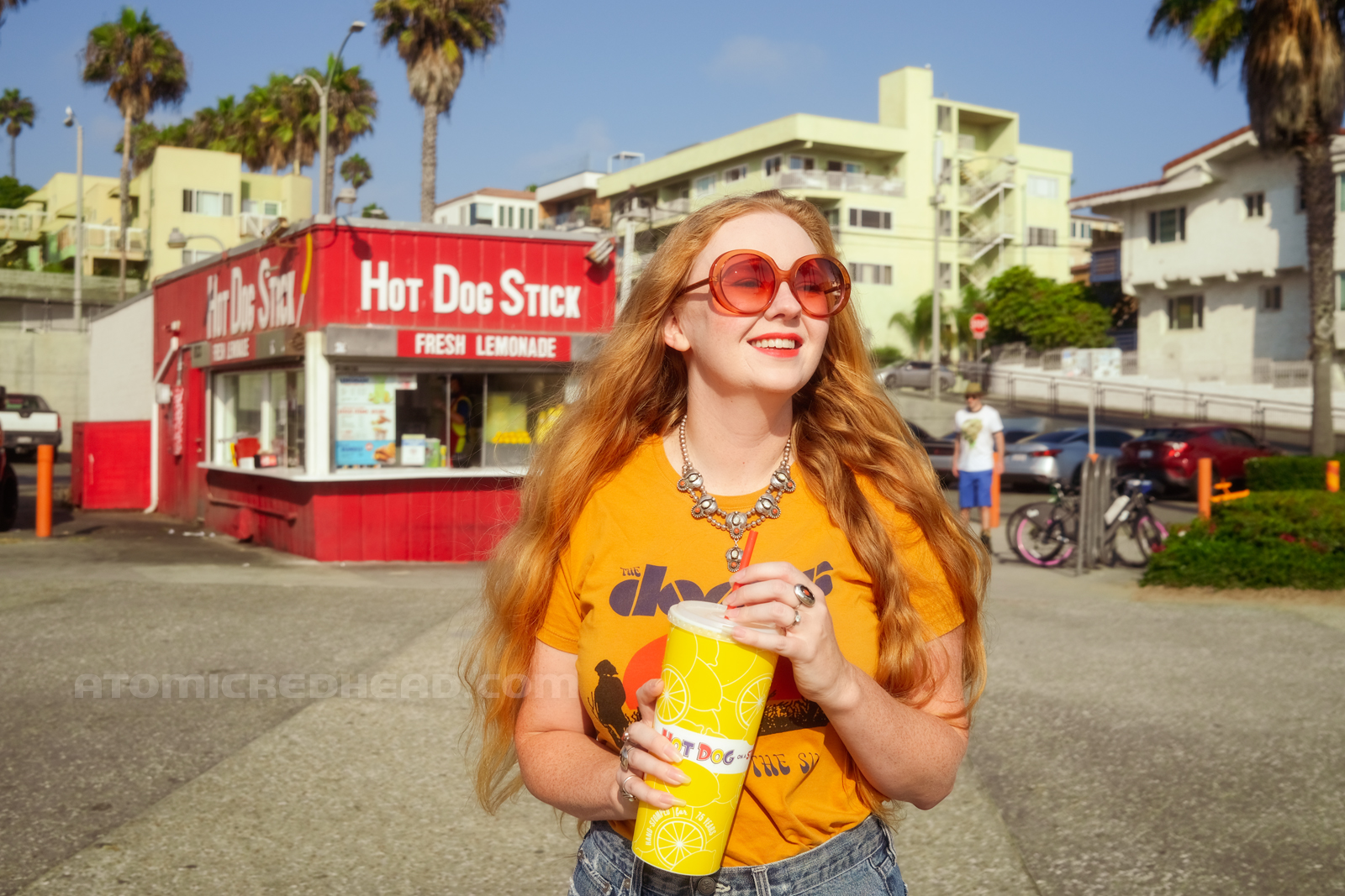 Myself, wearing a yellow shirt featuring the band The Doors, standing in front of Hot Dog on a Stick holding a cup of lemonade.