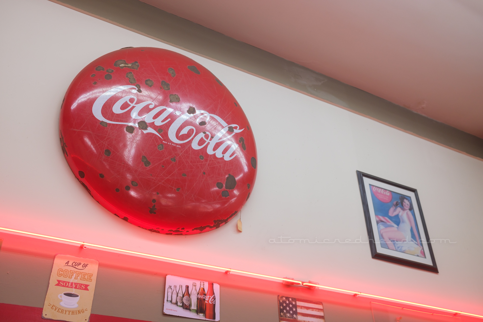 A large circular sign reads "Coca-Cola" in their famous white script hangs above a stripe of red neon.