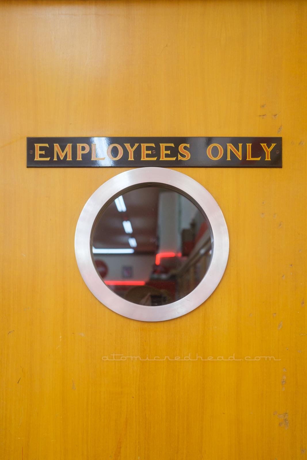 A wood door features a porthole style window with a hand painted sign above reading "Employees Only"