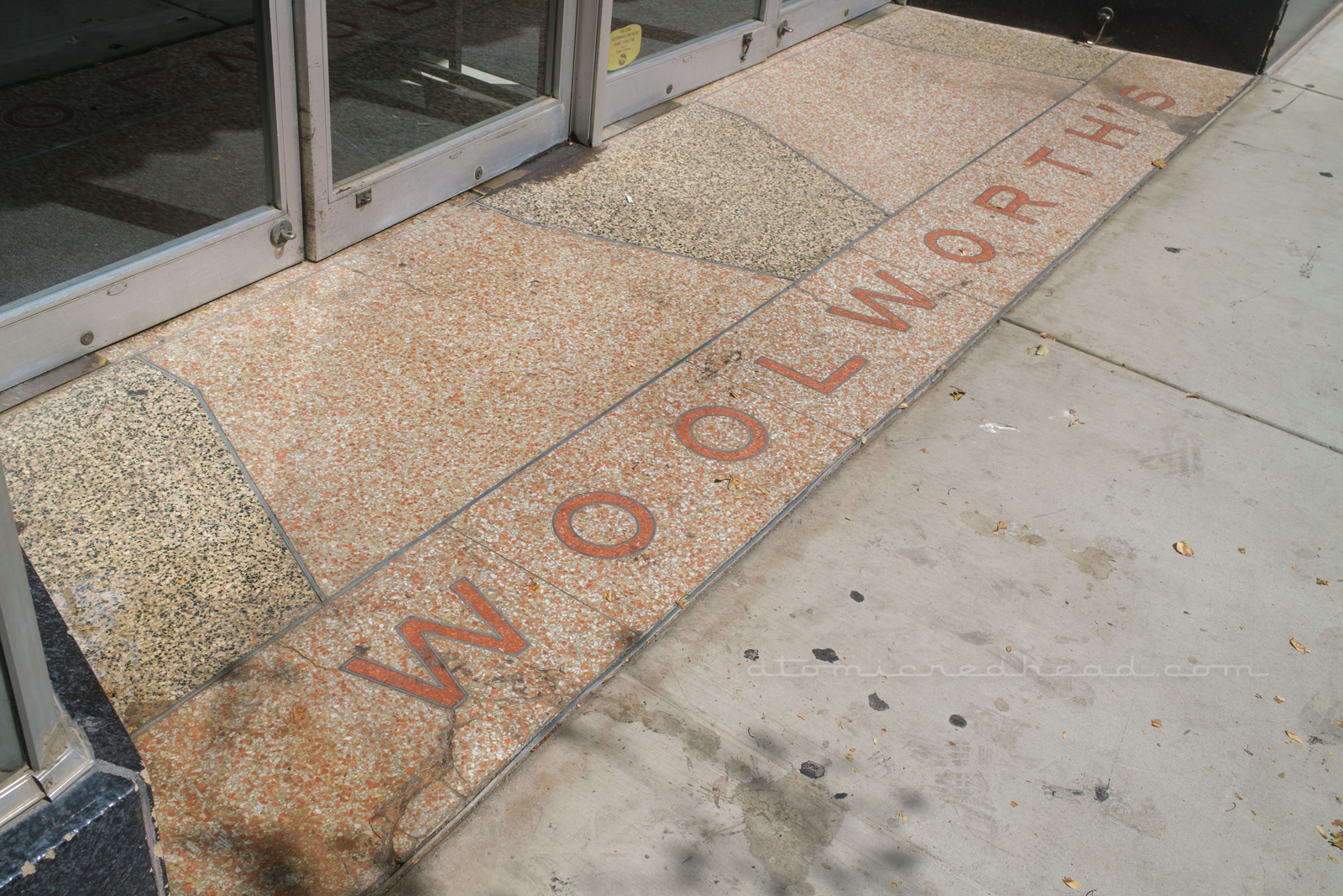 Cream, brown and red terrazzo reads "Woolworth's" outside the front doors.