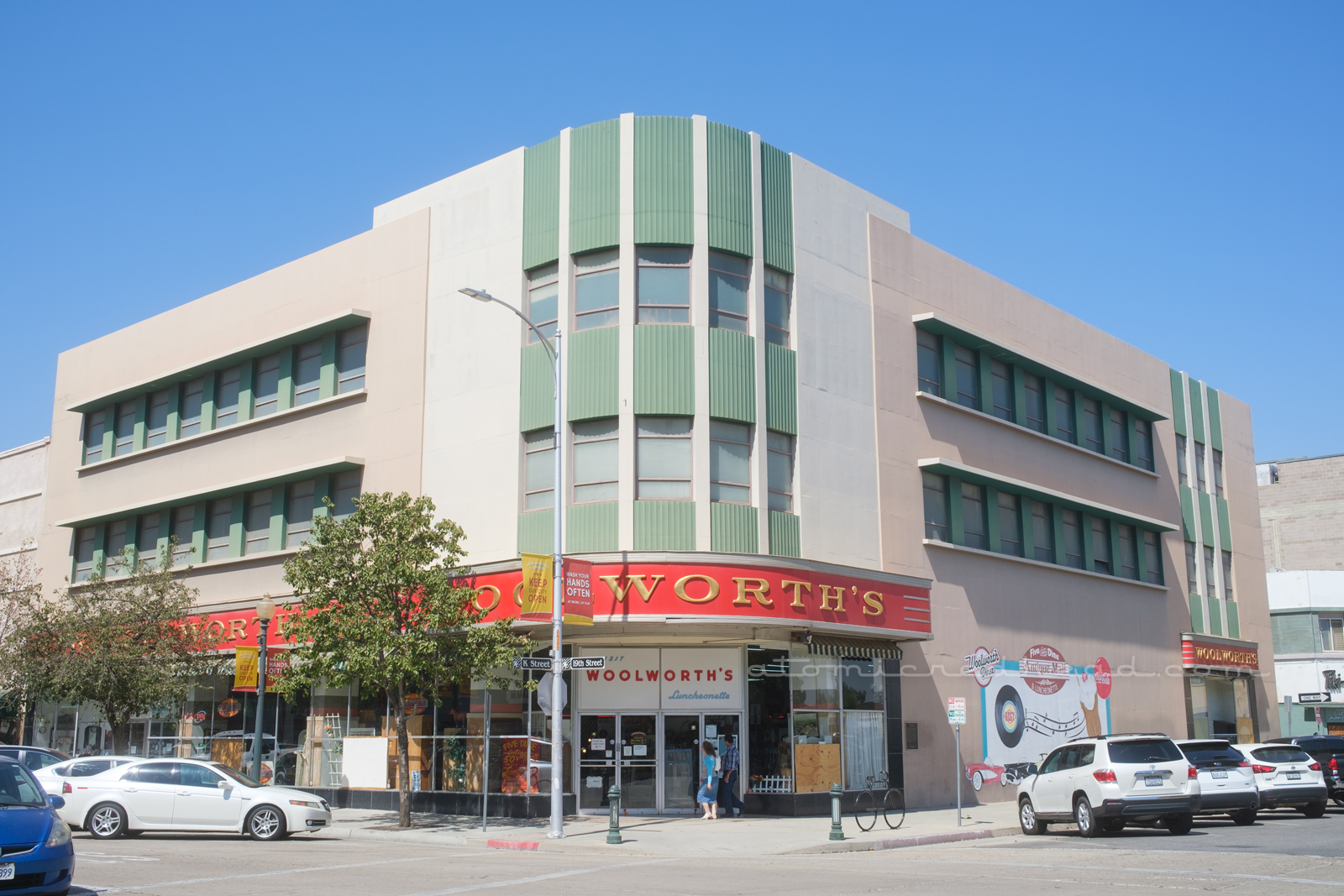 Overall of the Woolworth building. The corner is rounded with the massive red and gold "F.W. Woolworth's" sign coming around the curve. The upper floors painted a pale tan, with cream and mint details.