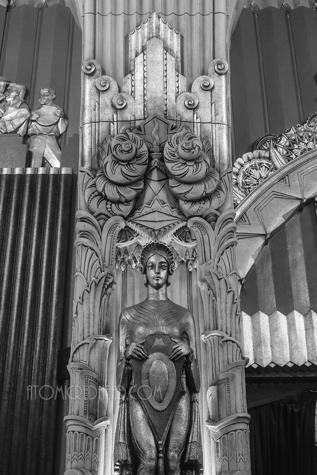 Black and white photo of an Art Deco stylized maiden statue holding a shielf.