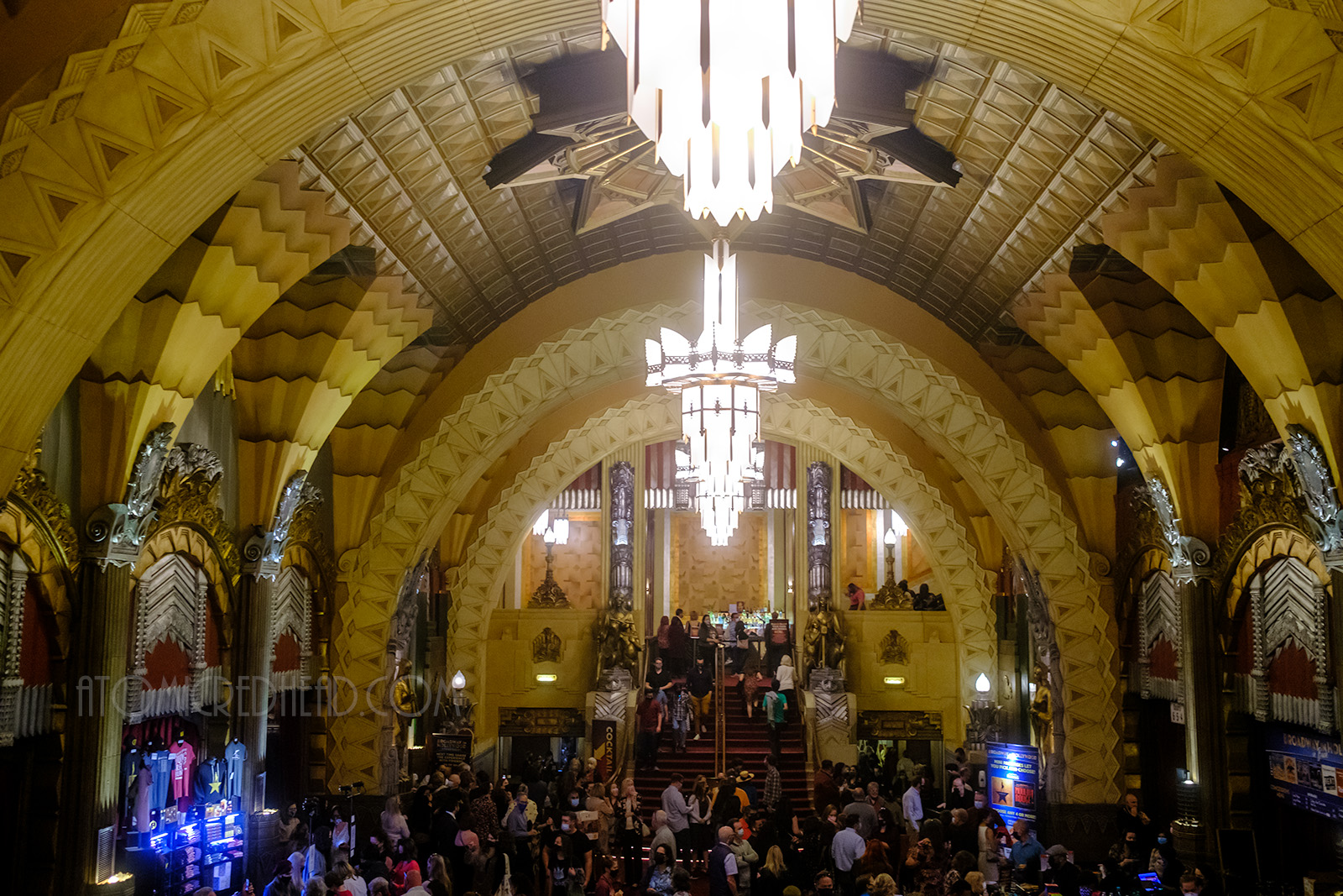 Overall view of the lobby, which features an arched ceiling with colorful decorative elements. In the middle hang three chandeliers of gold metal and white glass.