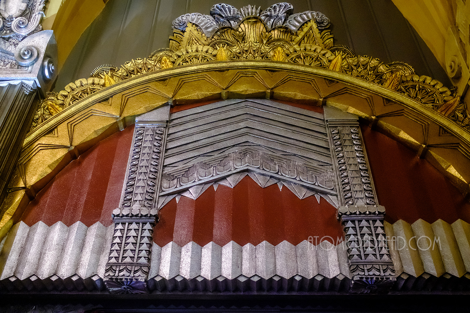 Various Art Deco details of an arched gold design, a gate like silver design, with red backing.