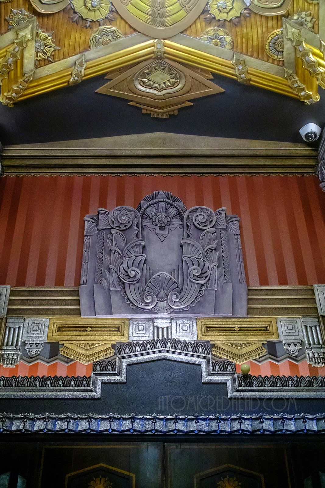 An intricate silver Art Deco style relief sits above a doorway with a red backing and gold details below.
