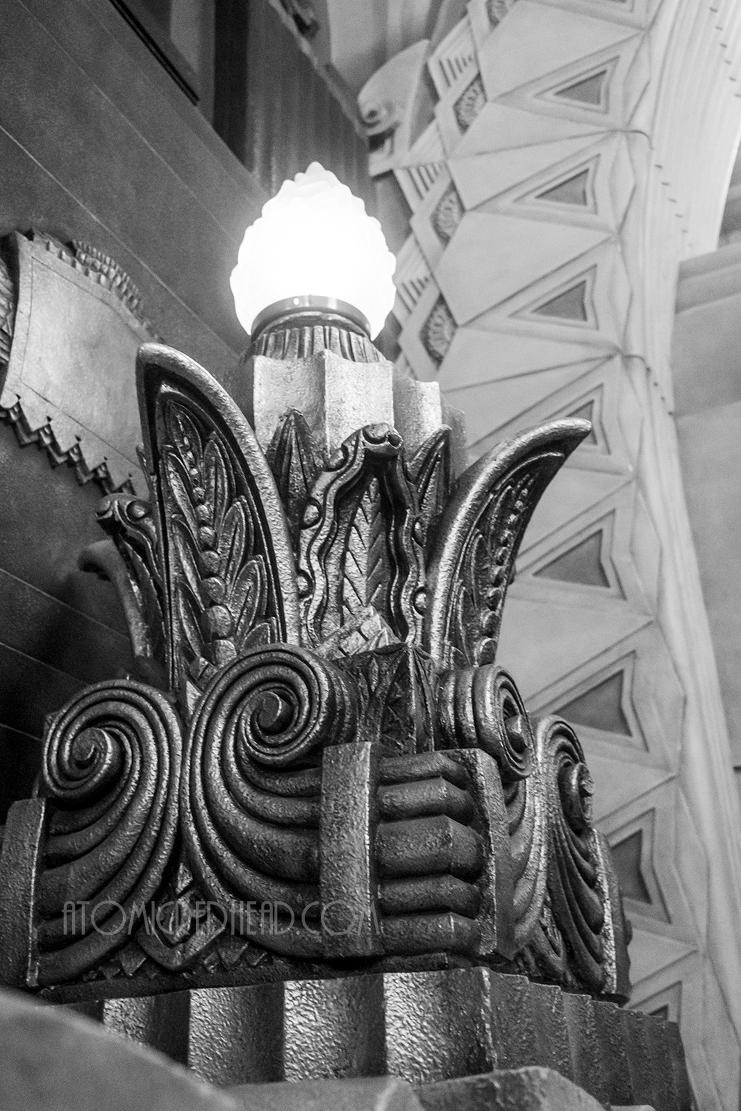 Black and white image of a light fixture that has a flame like glass shade popping out of an Art Deco stylized leaf like base.