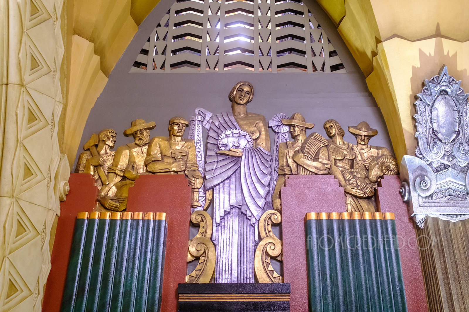 A gold and silver woman holds the California seal, with gold people behind her displaying the various agriculture elements of California.