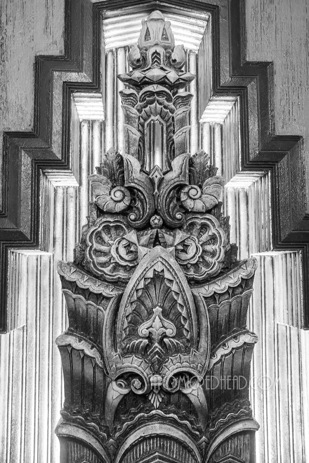 Black and white photo of a tiered Art Deco sculpture feating shell like designs, and laurel leaf like elements along with curls and waves. 