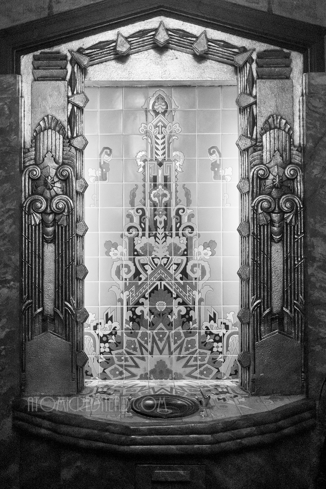 Black and white photo of an Art Deco style image on tile that is flanked by relief work done in a swirling Art Deco motief.