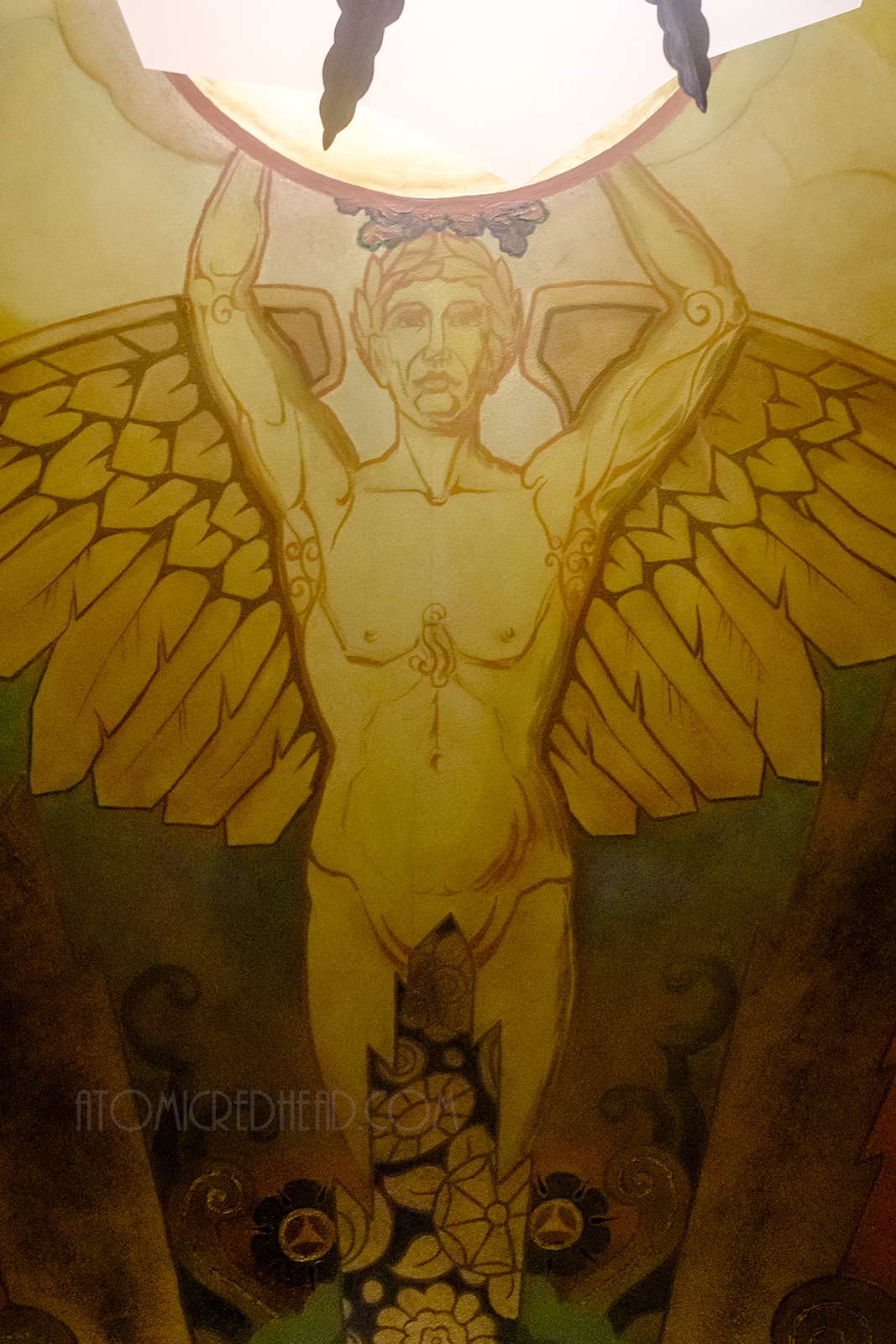 A painting of winged Icarus holding a glass light fixture on the ceiling.