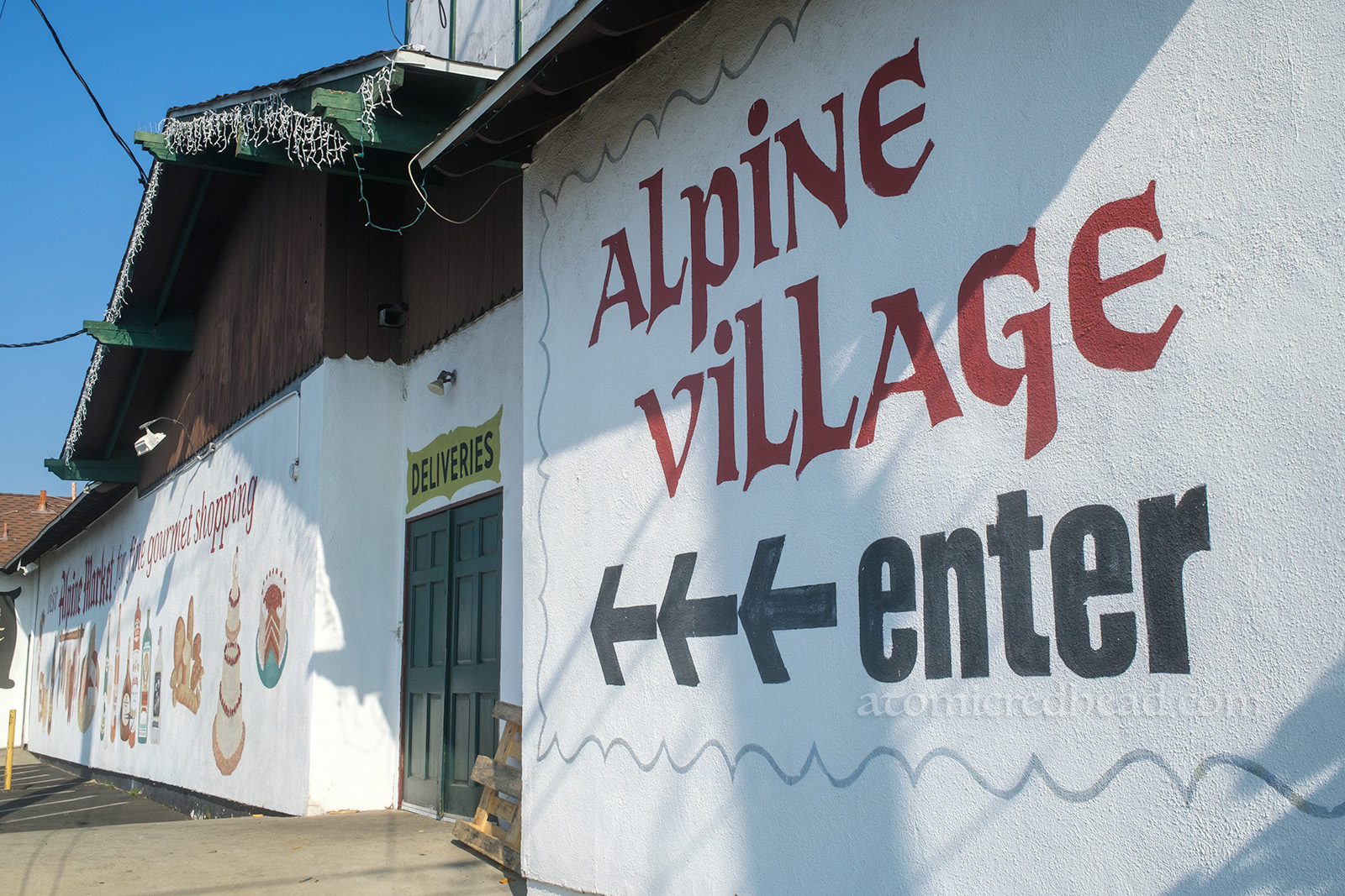 Painted on the sign of a chalet style building reads "Alpine Village enter"